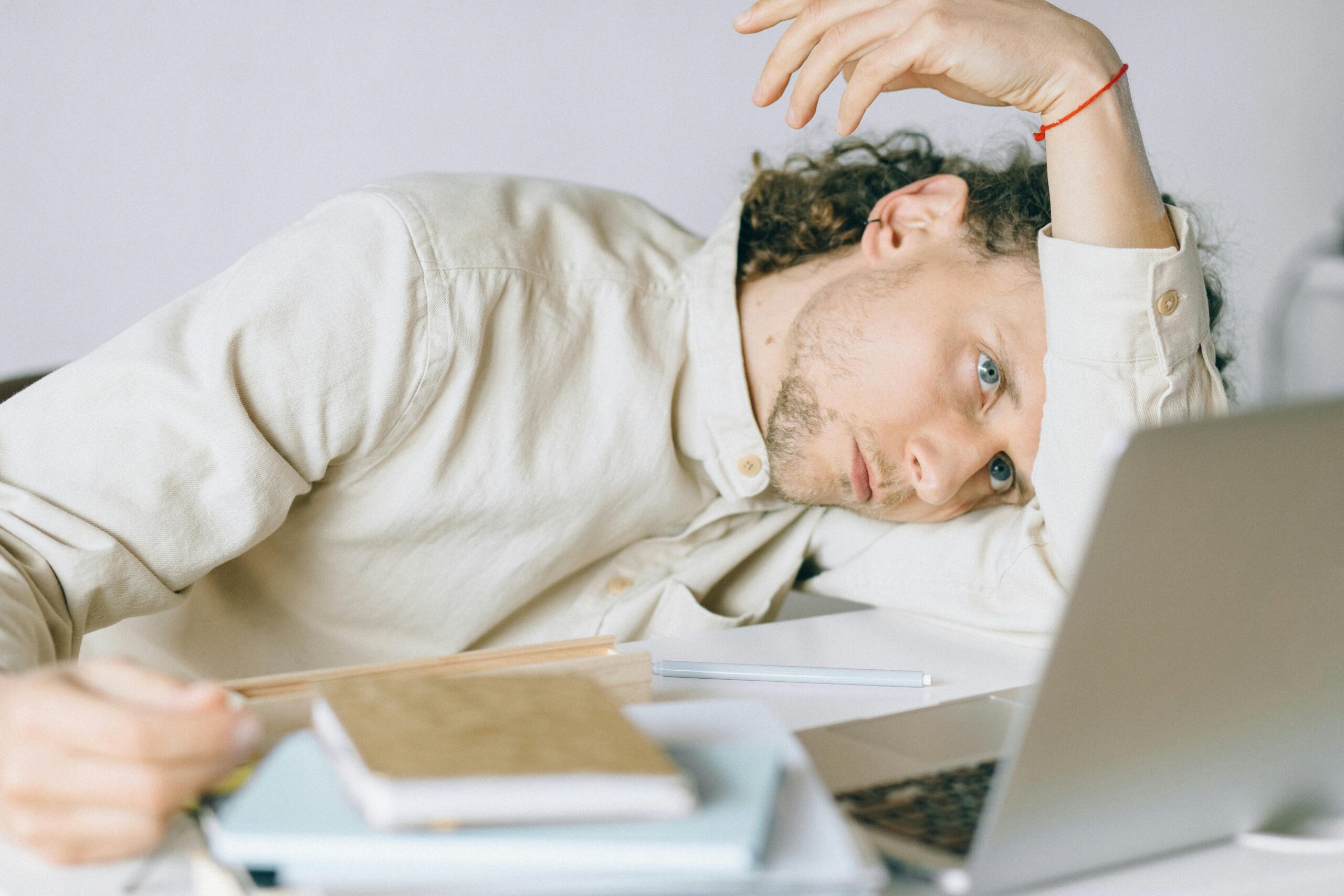 A stressed person sitting at a desk buried under piles of paperwork labeled 'Loan Deferment Documents'